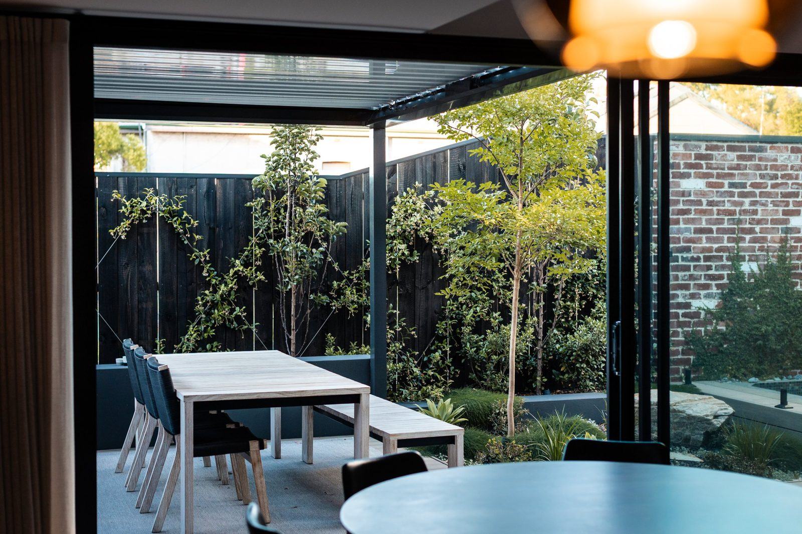 Covered alfresco dining looking onto a courtyard of trees and star jasmine against charred timber fencing