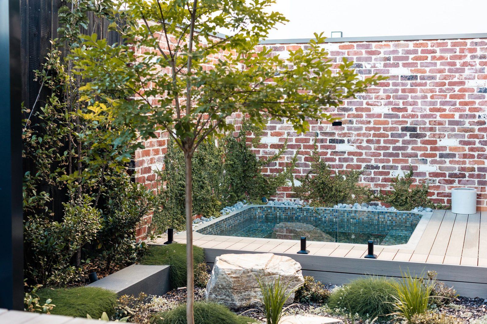 Mosaic-tiled plunge pool on a timber deck against a recycled brick wall with climbing fig