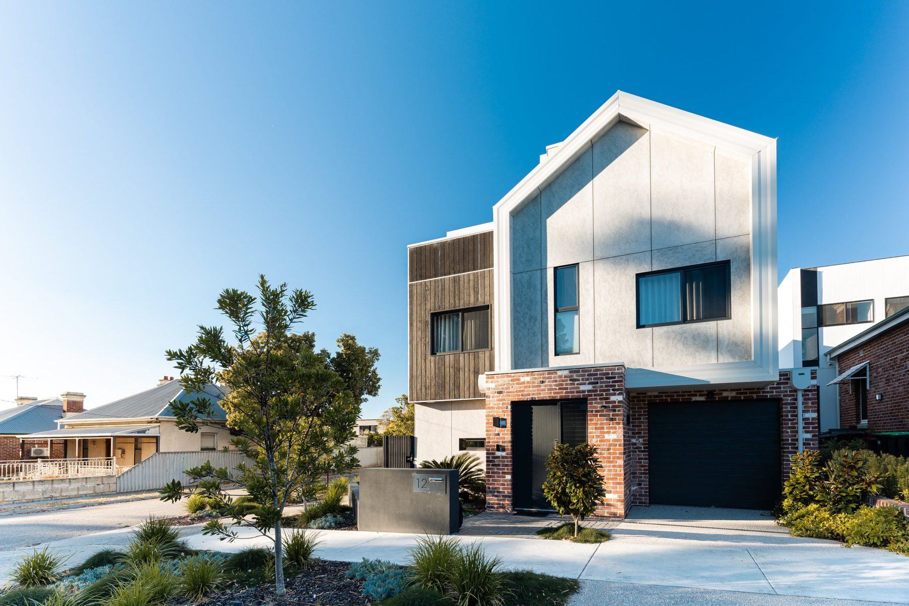 Claverton Residence: gabled facade in render, charred timber and recycled brick behind a native verge garden