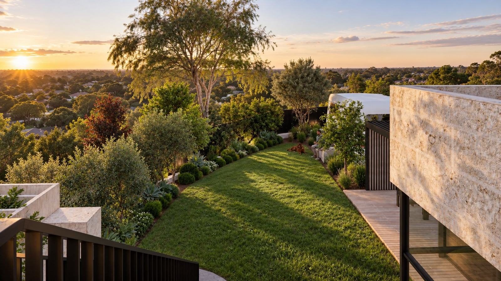 Lawn edged with layered planting running to a sunset view over the treetops, beside the limestone extension and timber deck