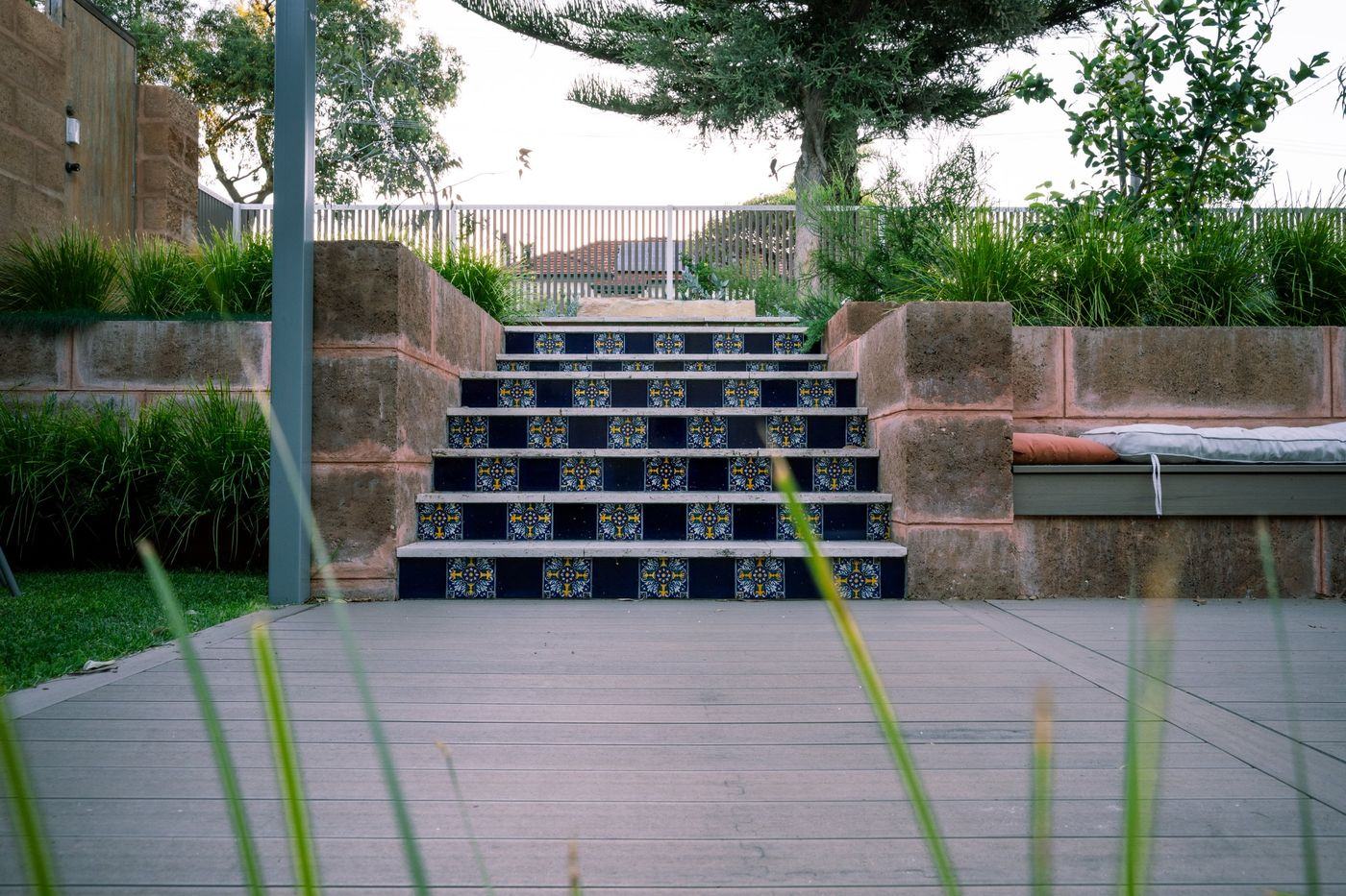Patterned blue and yellow tile stair risers between block retaining walls, rising from a deck to planted beds